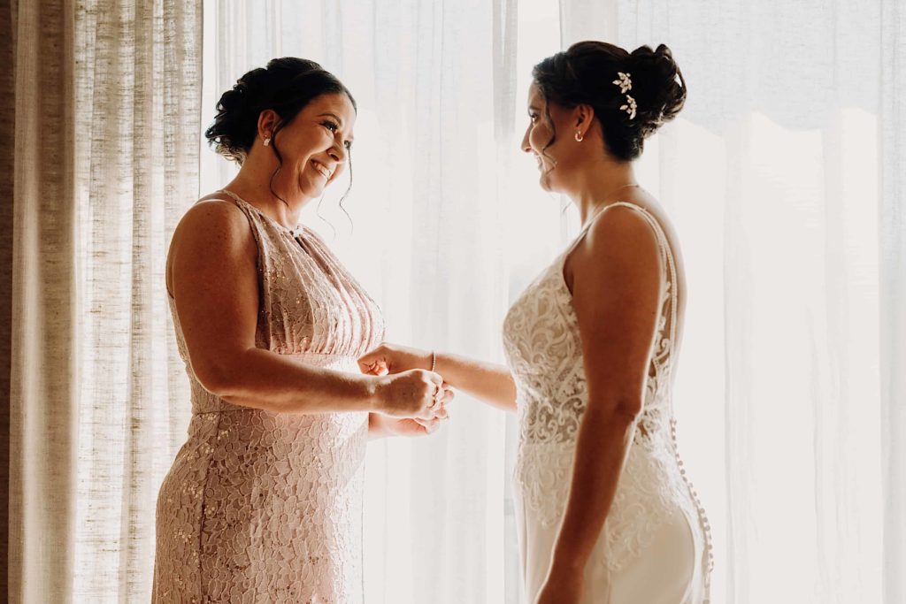mother and daughter getting ready for her wedding in front of a back lit window at Stonhurst at hampton valley connecticut wedding venue by ladman studios