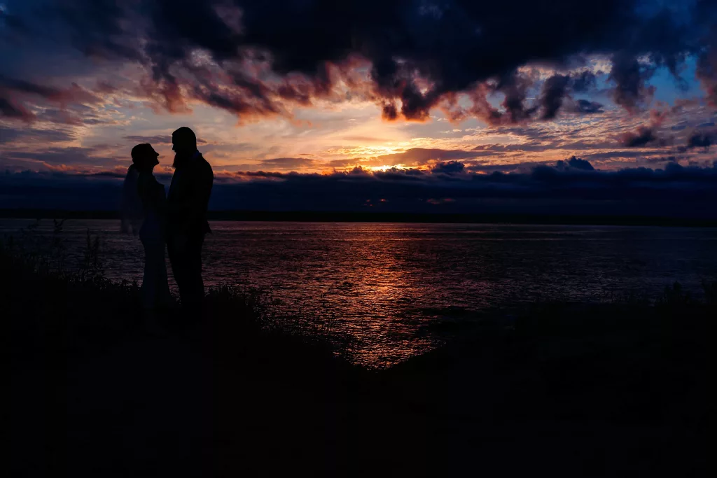 couple standing at the edge of the water looking at each over during sunset