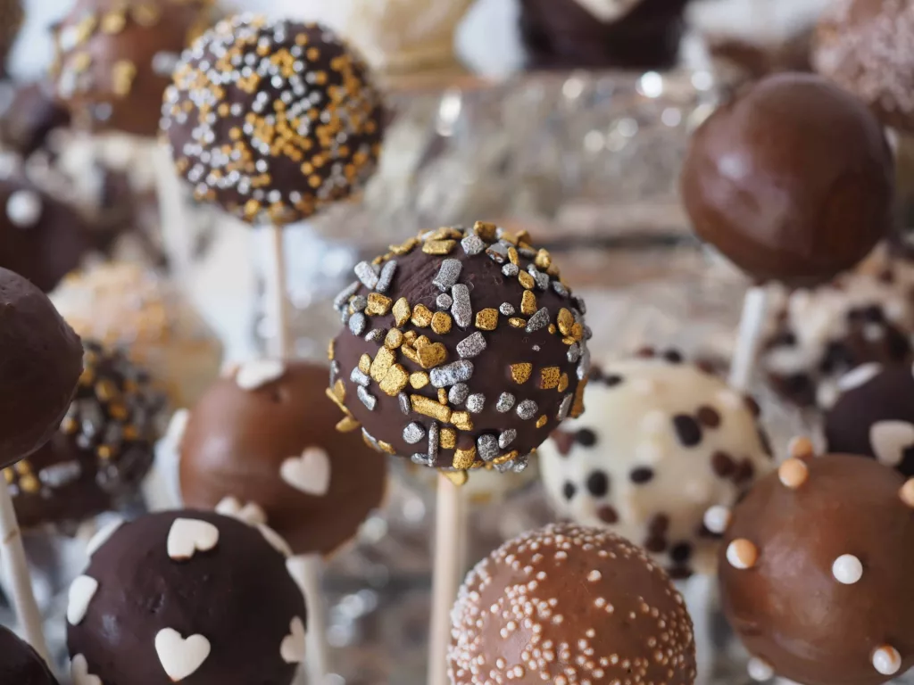 Delicious and colorful cake pops arranged on a platter with sprinkles and decorations. Each bite-sized treat features a moist cake center, coated in chocolate and topped with different festive designs, perfect for any celebration or sweet craving