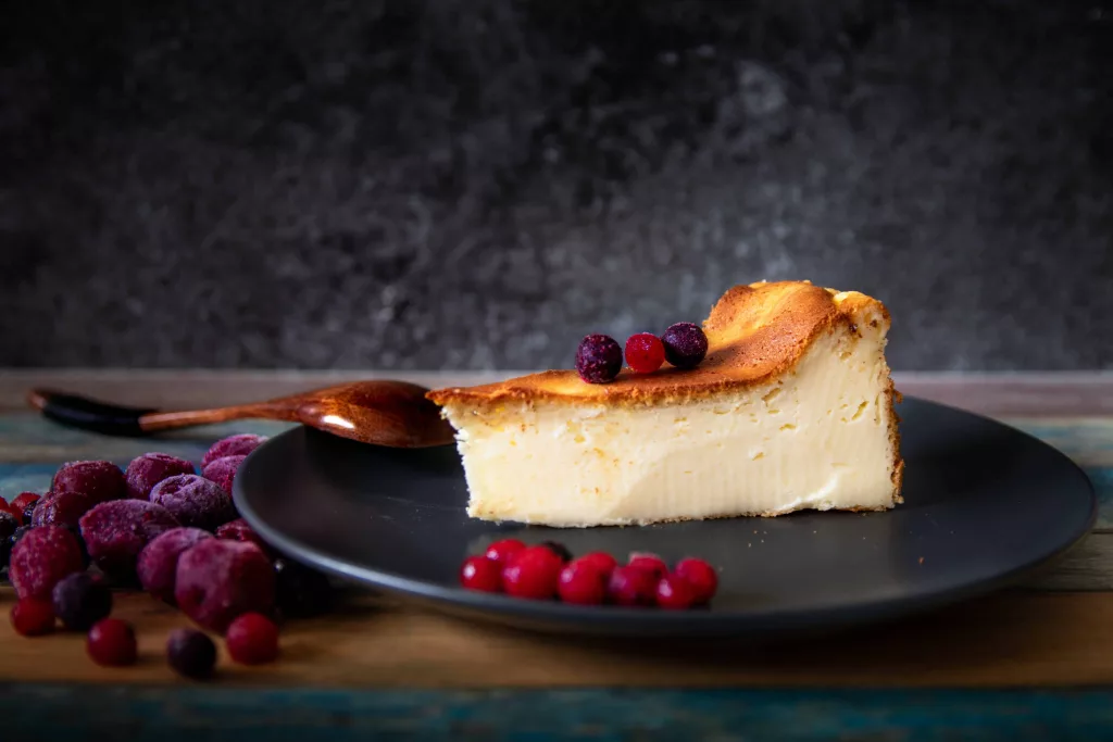 Delicious cheesecake on a black plate with berries and a wooden spoon.