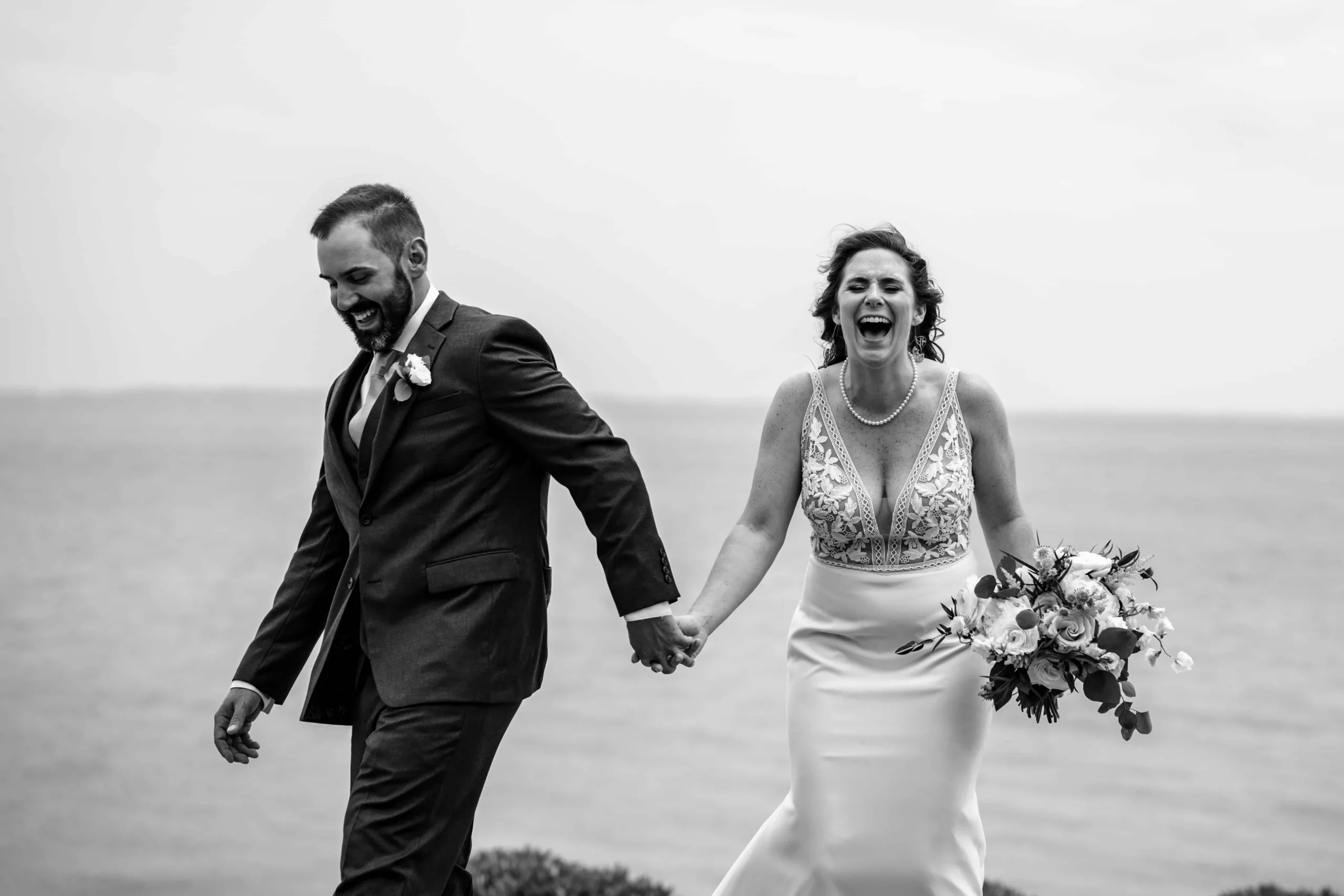 A laughing couple in wedding attire, holding hands as they walk.