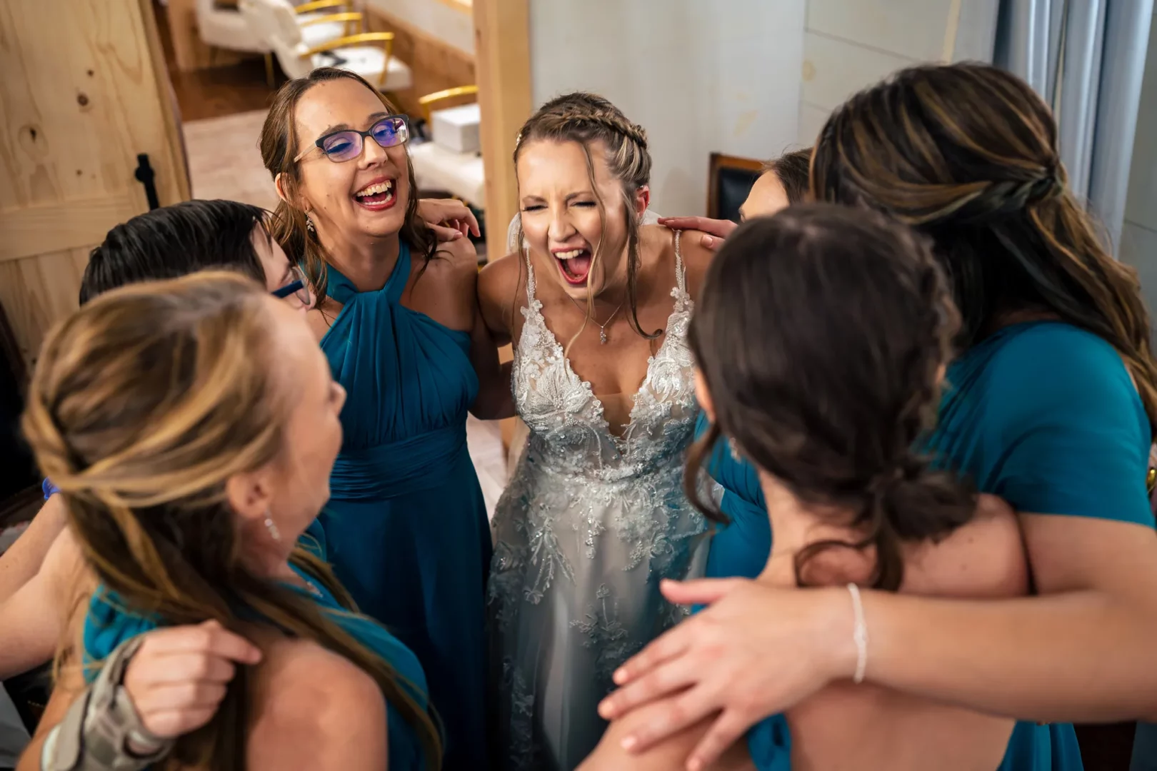 A bride laughs joyfully while surrounded by her bridesmaids in matching teal dresses, taken by a Connecticut wedding photographer.