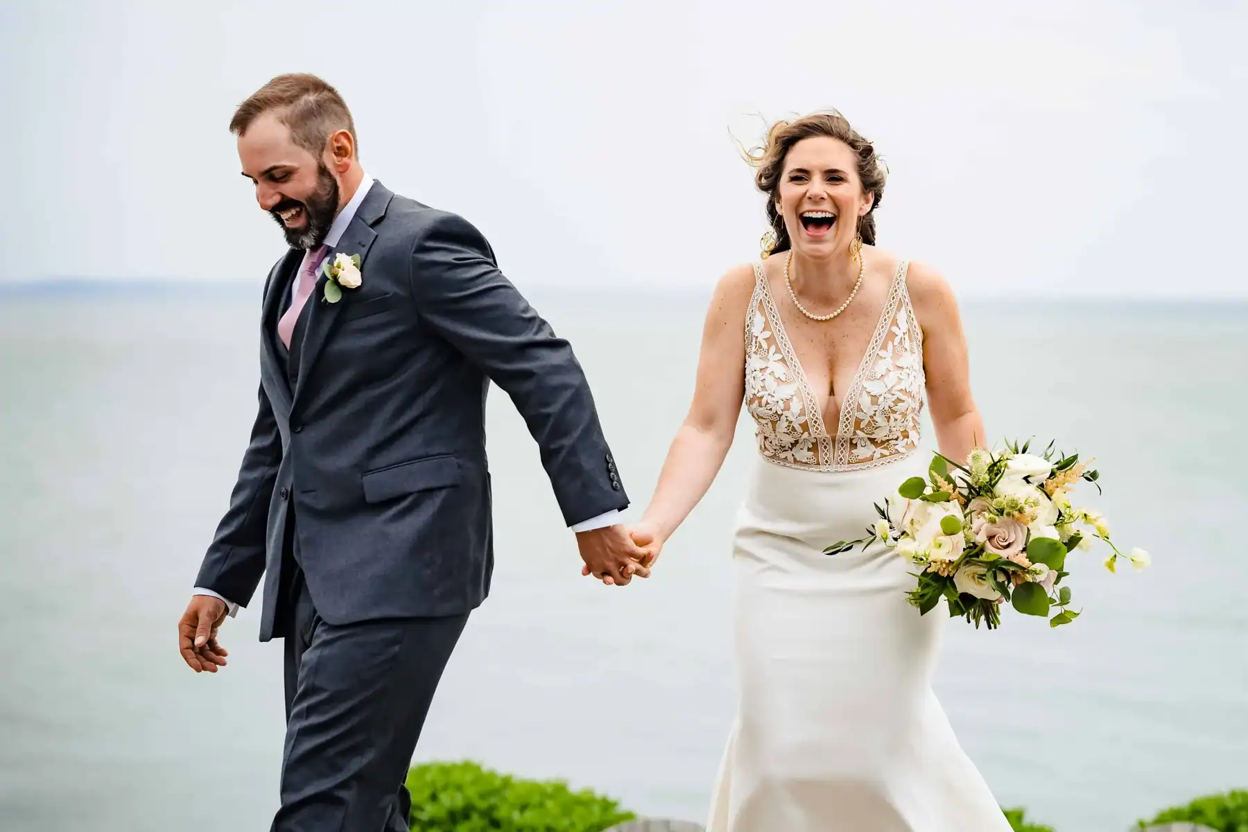 Bride and groom laughing and holding hands by the ocean, captured by Ladman Studios, a Connecticut wedding photographer helping couples find their ideal match through expert wedding photography guides.