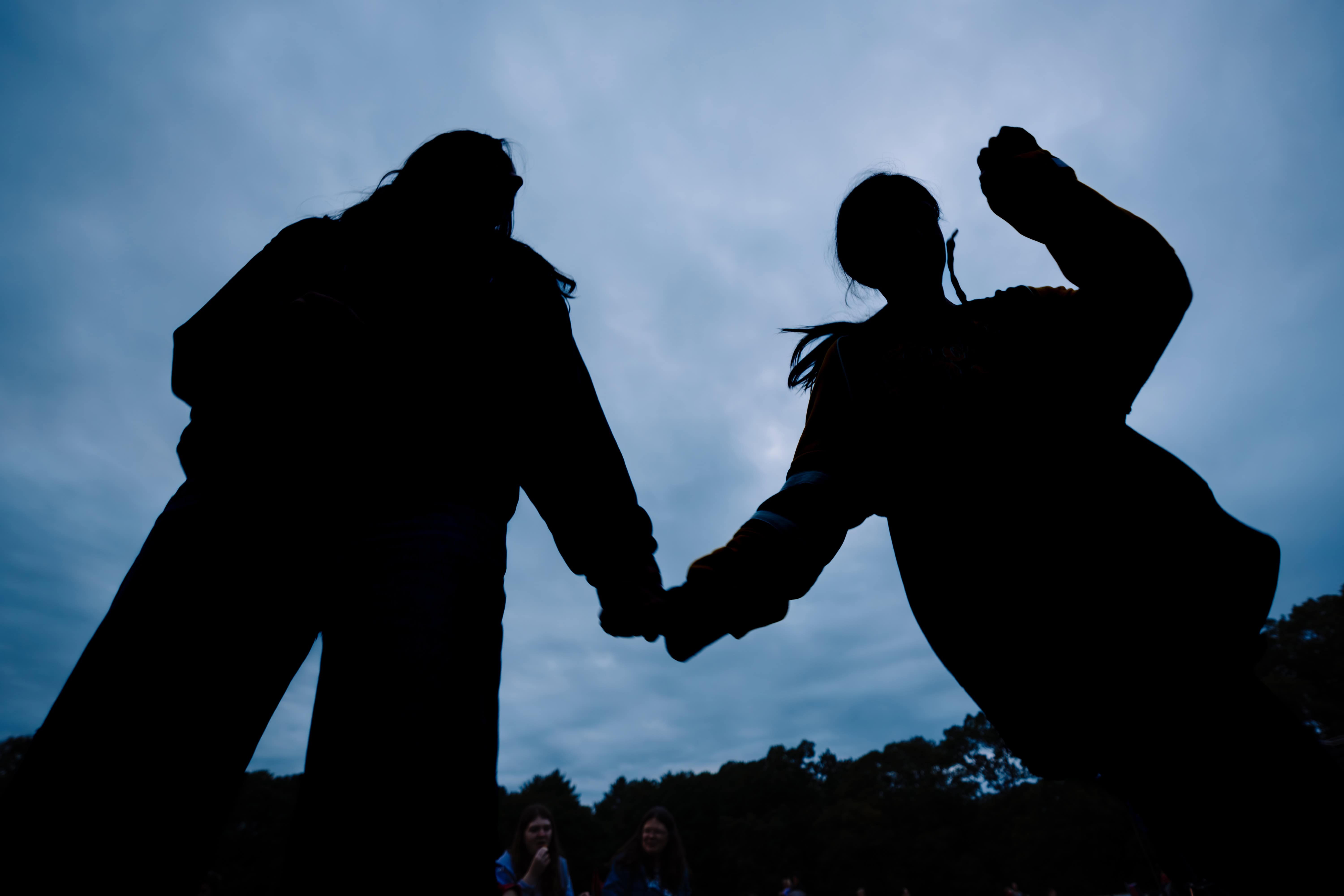 A silhouette of two kids holding hands and playing outdoors at dusk, captured in a Connecticut documentary family photography session.